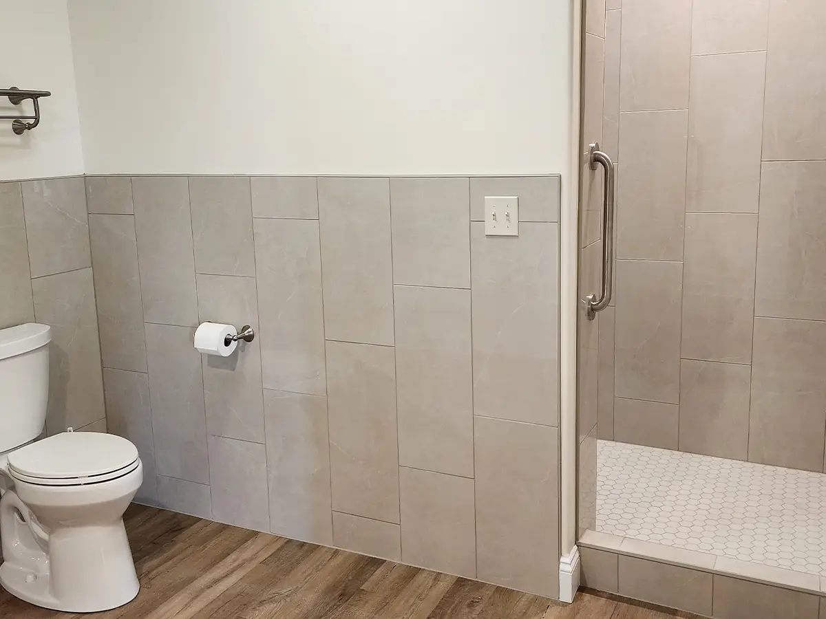 basement remodeling small bathroom with gray tile, vinyl wooden pattern floor, white walls and walk-in shower