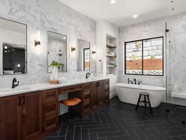 Large modern bathroom black tile pattern floor, wood cabinets and white countertops. 3 mirrors and 2 sinks