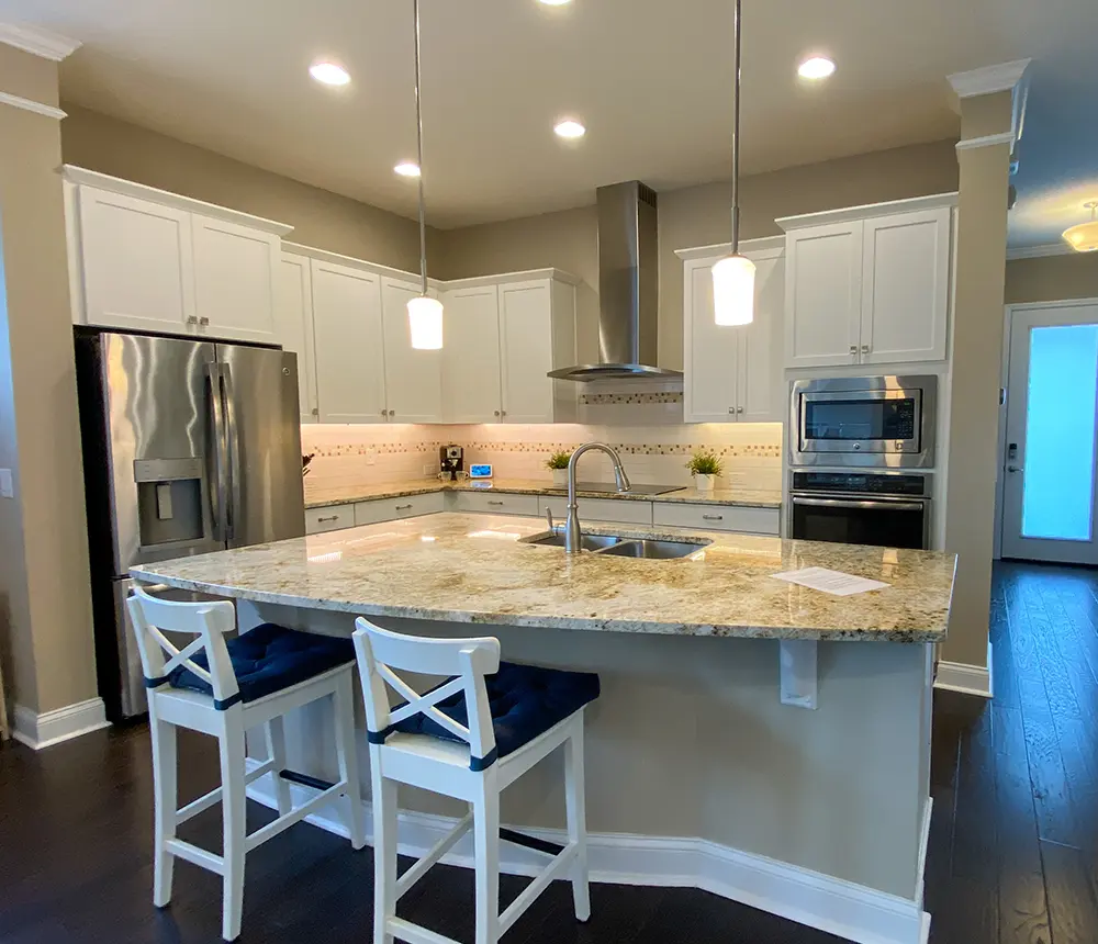 New modern remodeled kitchen, gray beige walls, spot-on lights, white cabinets and kitchen island with sink and bar chairs