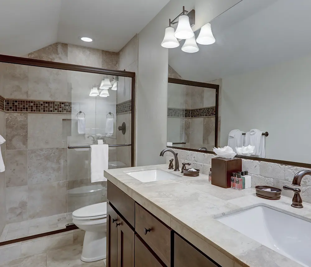 new modern small bathroom with brown wooden cabinets with marble pattern countertop, double vanity sinks and walk-in shower