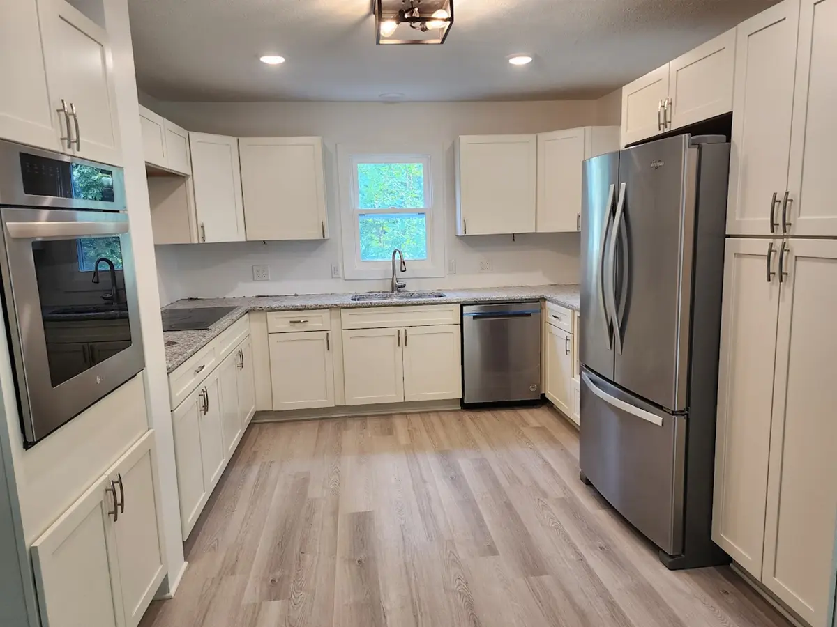 kitchen remodeling after the renovations, wooden floor, built-in oven and dishwasher, white cabinets with gray marble countertops